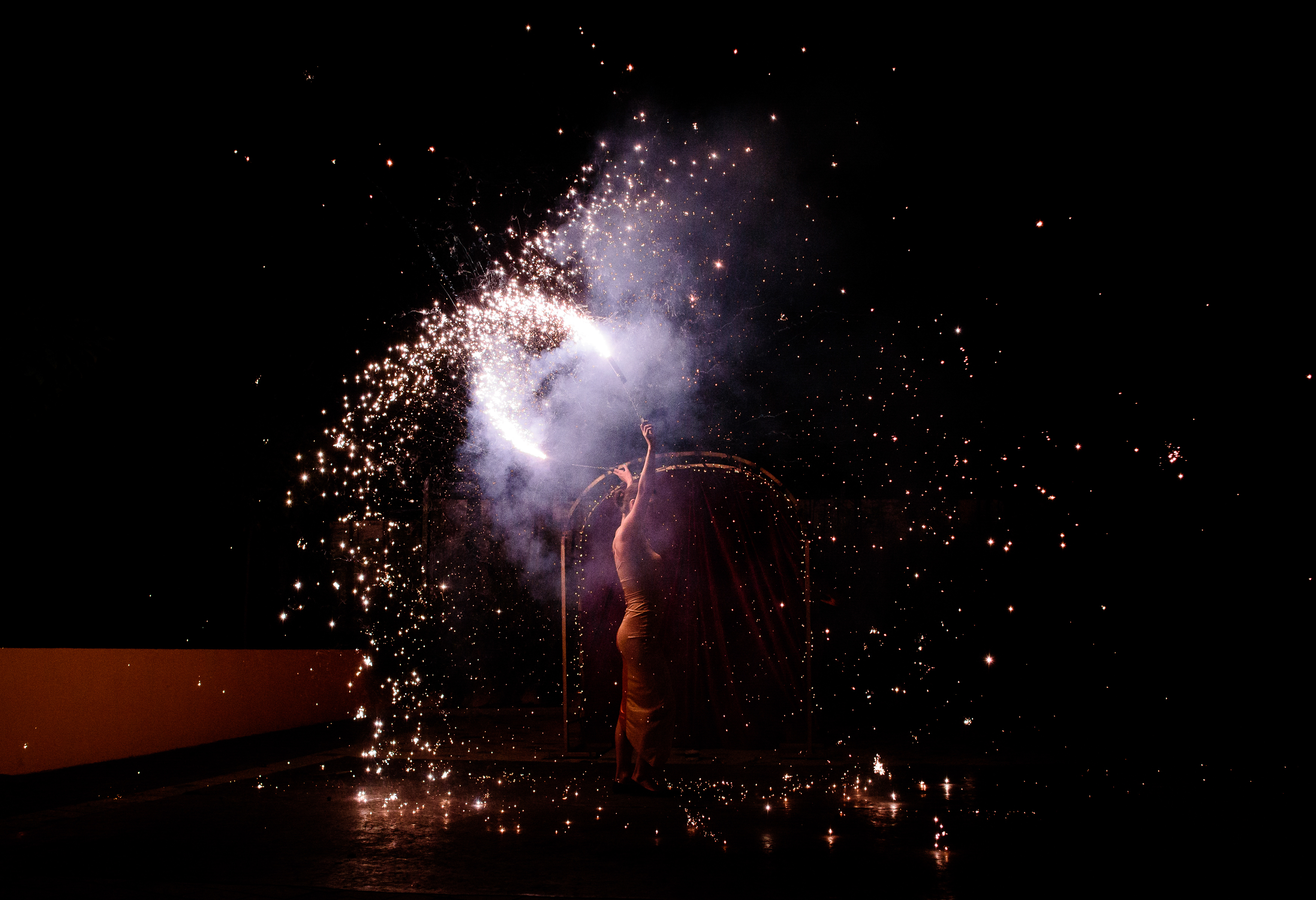 Girl raises her hands with sparkling fire while she dances in the dark 