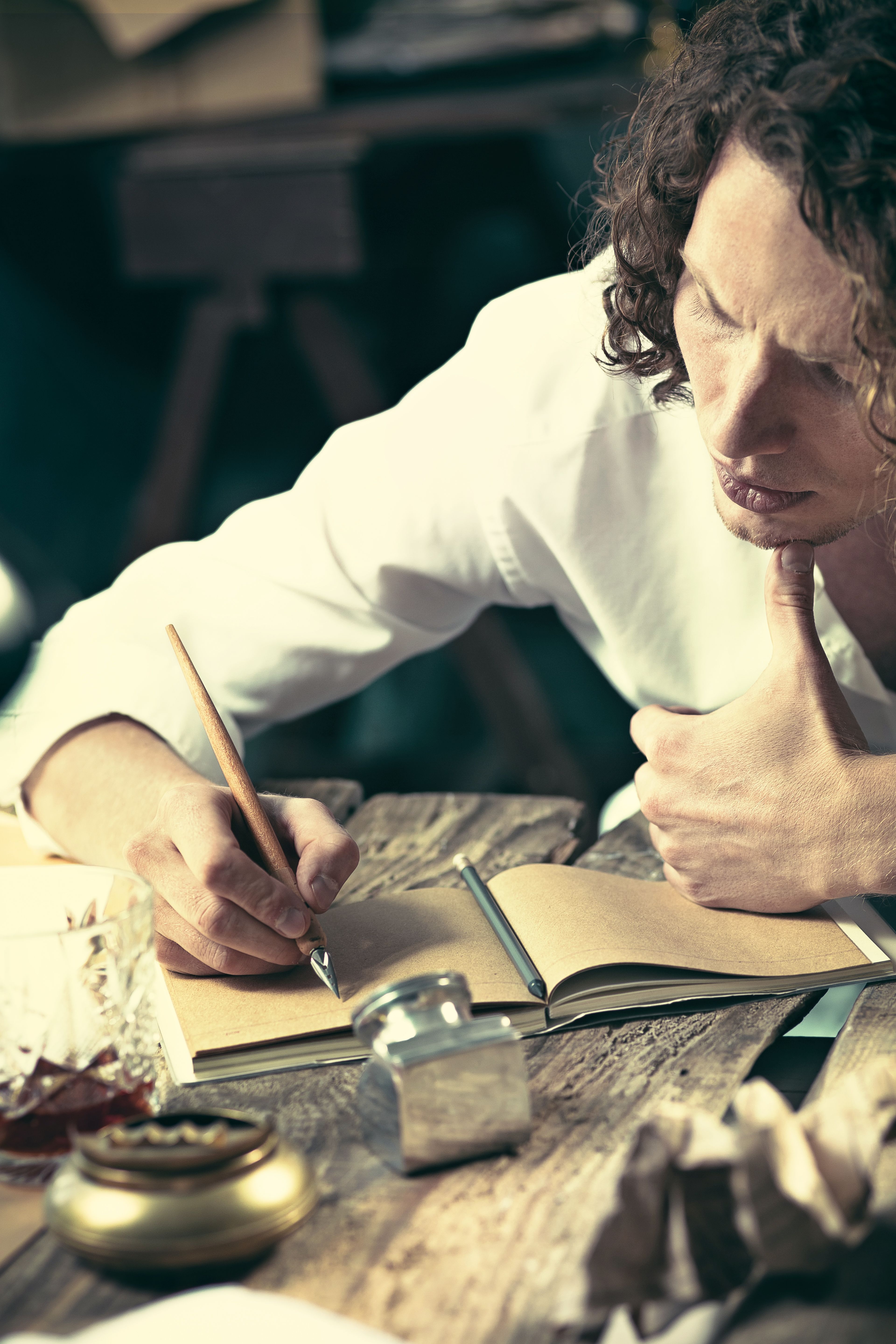 Writer at work. Handsome young writer sitting at the table and writing something in his sketchpad